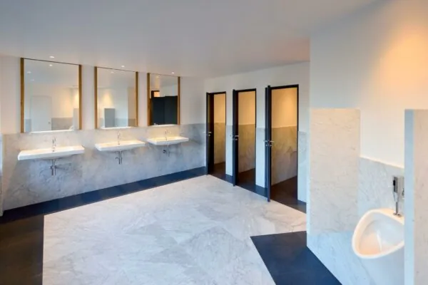 Ruime en modern afgewerkte openbare toiletruimte aan de Floris Grijpstraat met marmeren wanden, meerdere wastafels, toilethokjes en een urinoir.